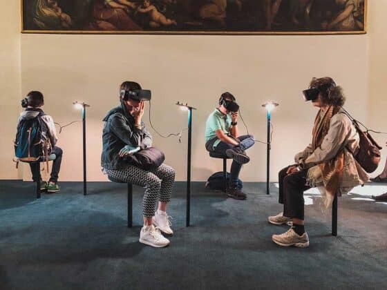 Vier Personen unterschiedlichen Alters sitzen in einem Museum vor einem riesigen Gemälde. Alle tragen VR-Brillen.