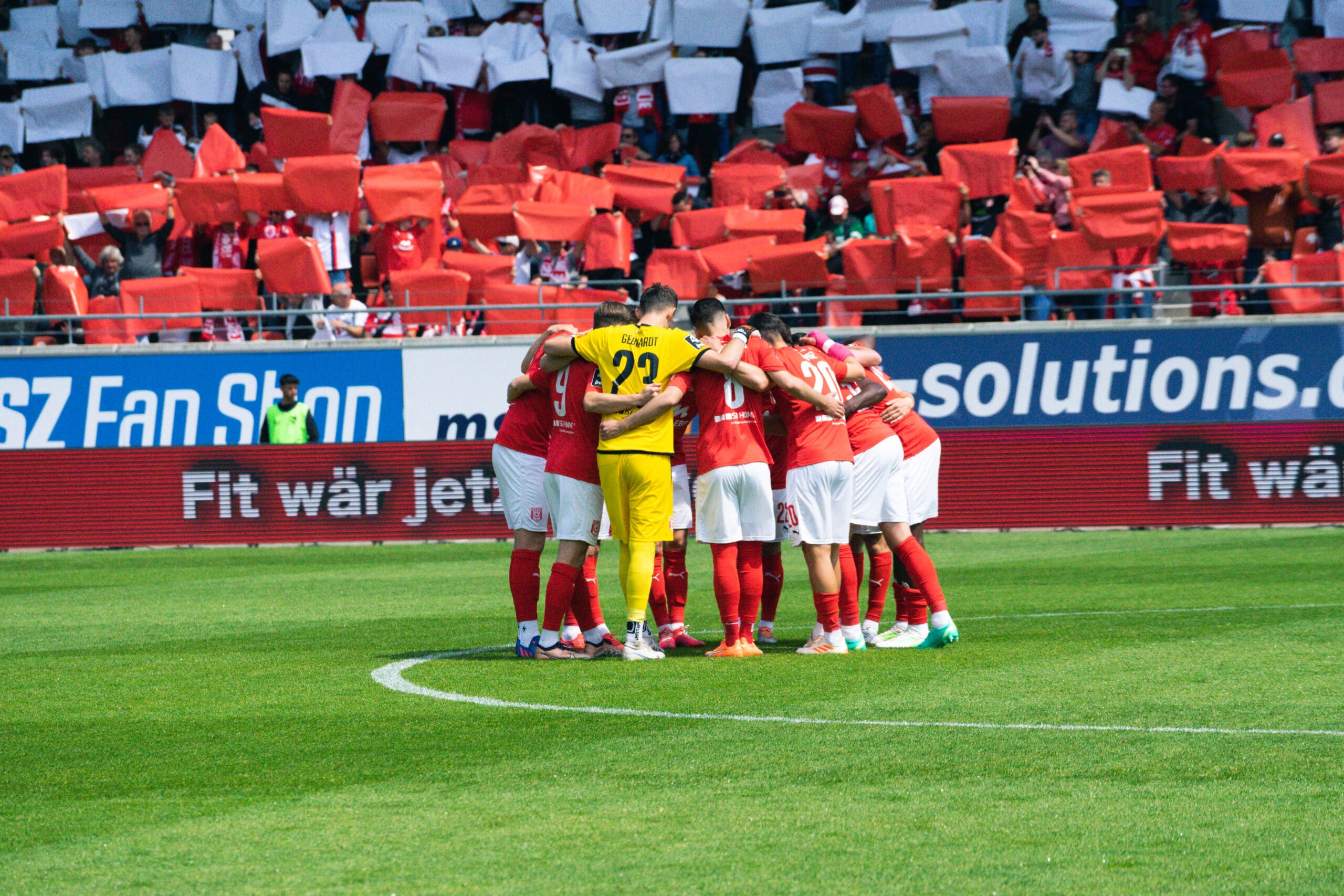 The players of the HFC in red and white stand in a circle for joint motivation for the upcoming match