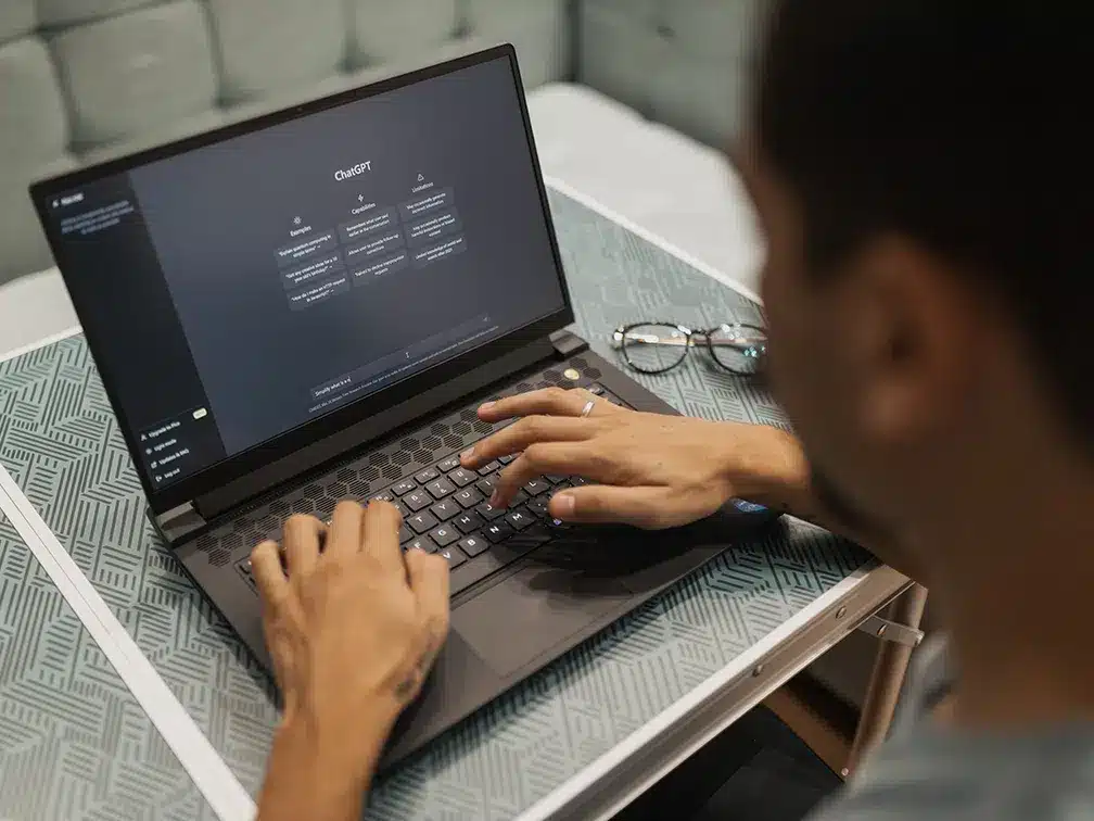 Looking over the shoulder of a young man sitting at a laptop with ChatGPT open