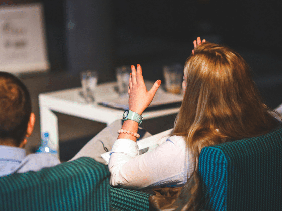 Woman from behind with long dark blond hair, raises her hands, sits on a petrol-coloured armchair