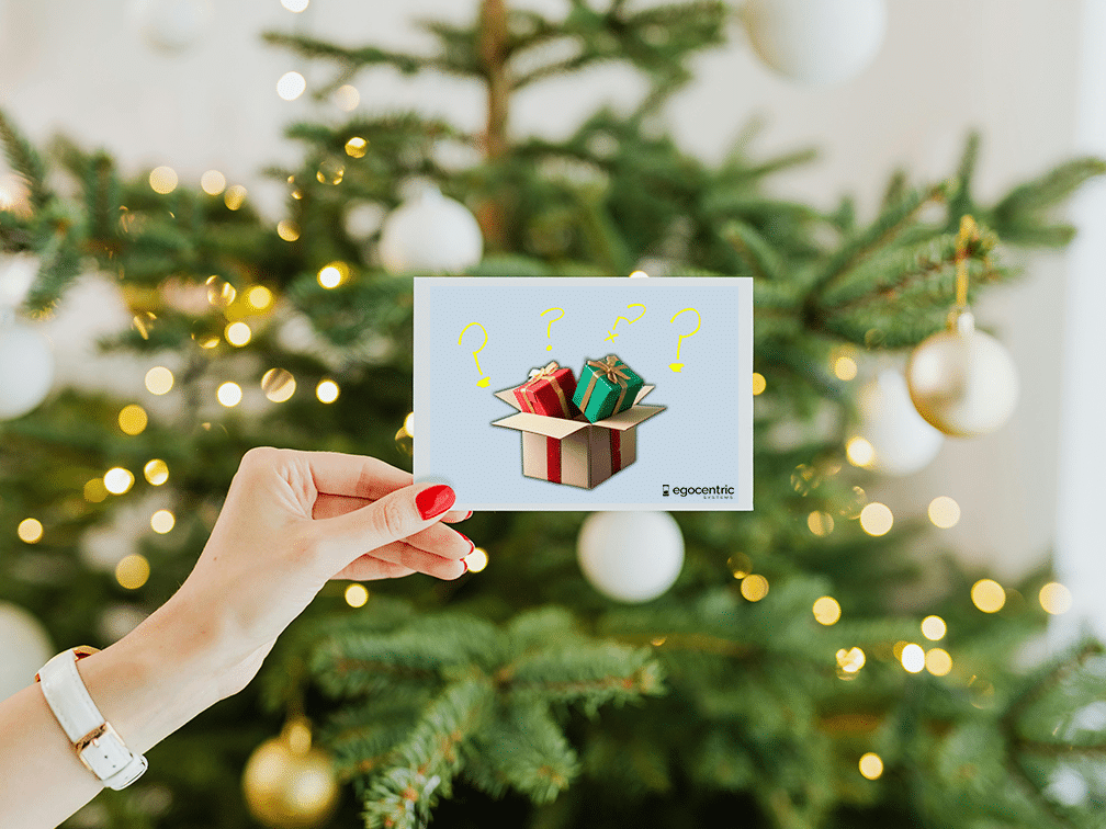 Hand in front of Christmas tree holding Christmas card with voucher