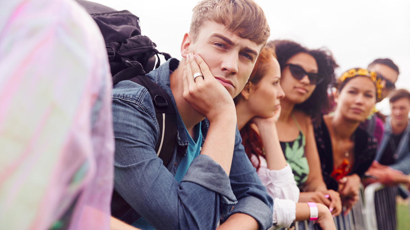 Gruppe junger Menschen, die leicht genervt hinter einer Barriere warten