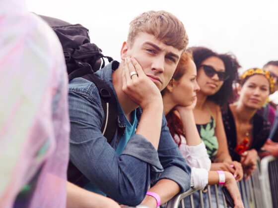 Gruppe junger Menschen, die leicht genervt hinter einer Barriere warten