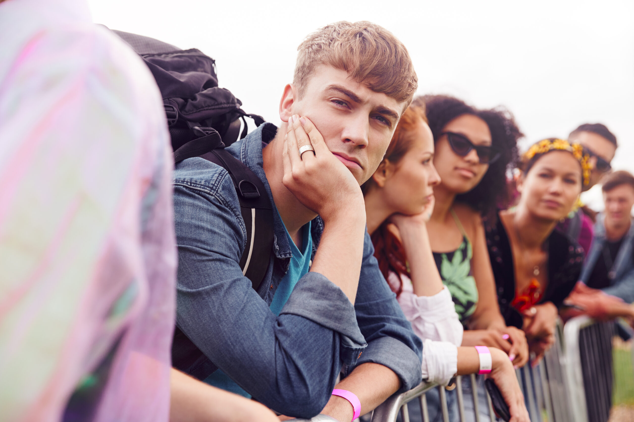 Gruppe junger Menschen, die leicht genervt hinter einer Barriere warten